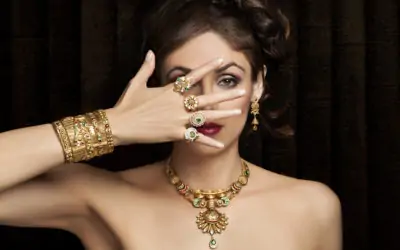 A woman showcasing intricate gold jewelry, partially covering her face with one hand.