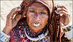 An elderly woman wearing traditional jewelry and a colorful shawl, adjusting her headscarf.