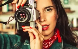 A woman holding a Praktica camera, posing for a photograph with a playful expression.