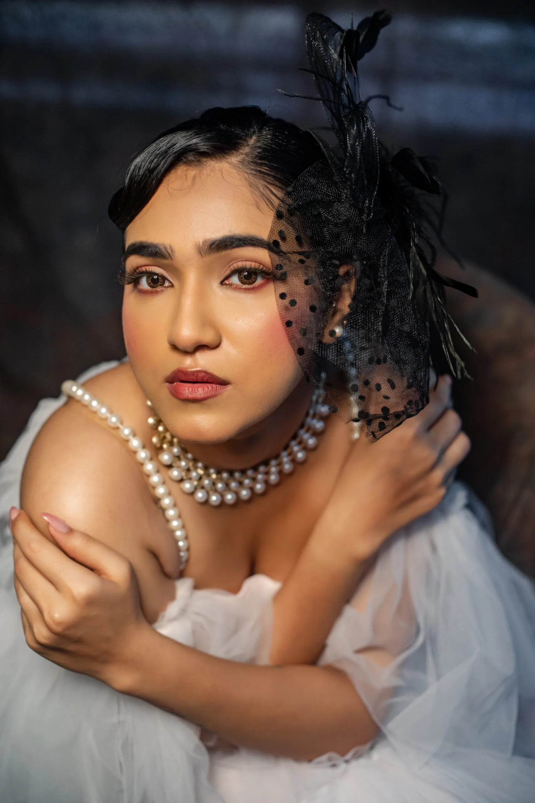 A woman in a white tulle dress adorned with pearls and a black fascinator.