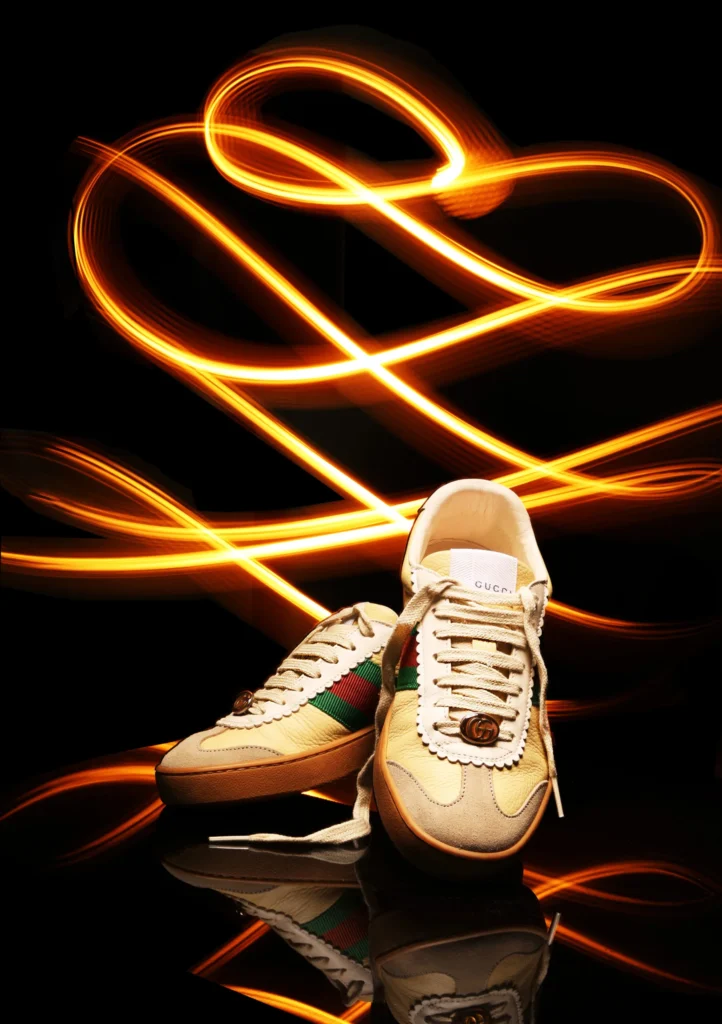 A pair of Gucci sneakers with intricate light painting swirls in the background.