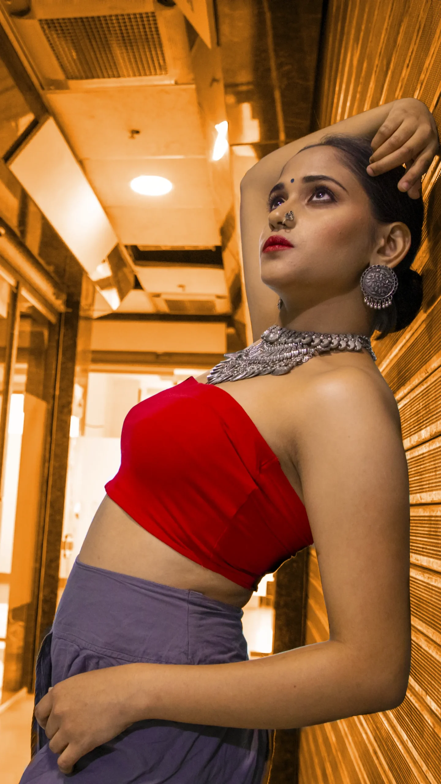 A woman in a vibrant red top and traditional jewelry striking a confident pose.