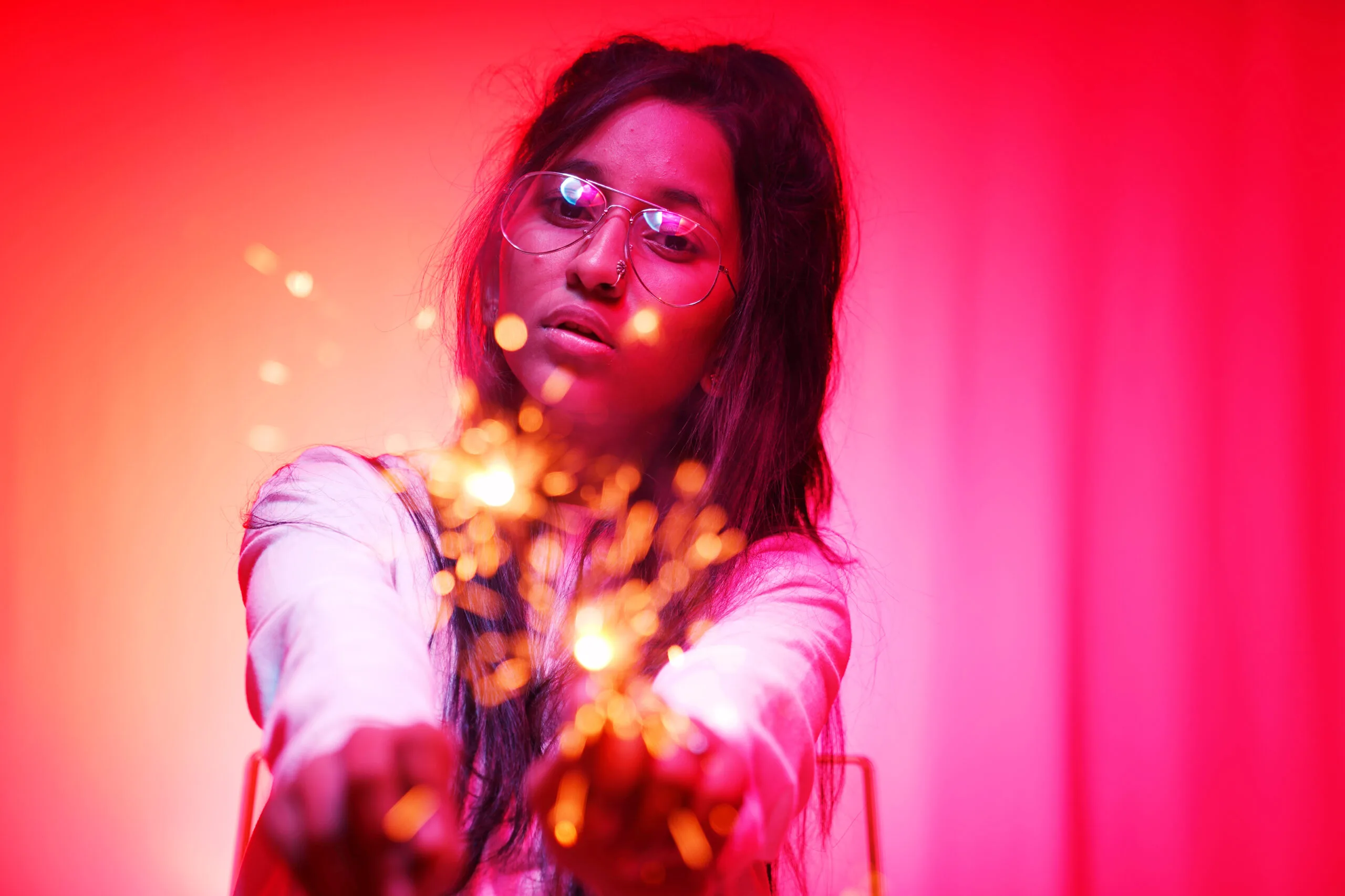 A young woman holding sparklers against a vibrant pink background.