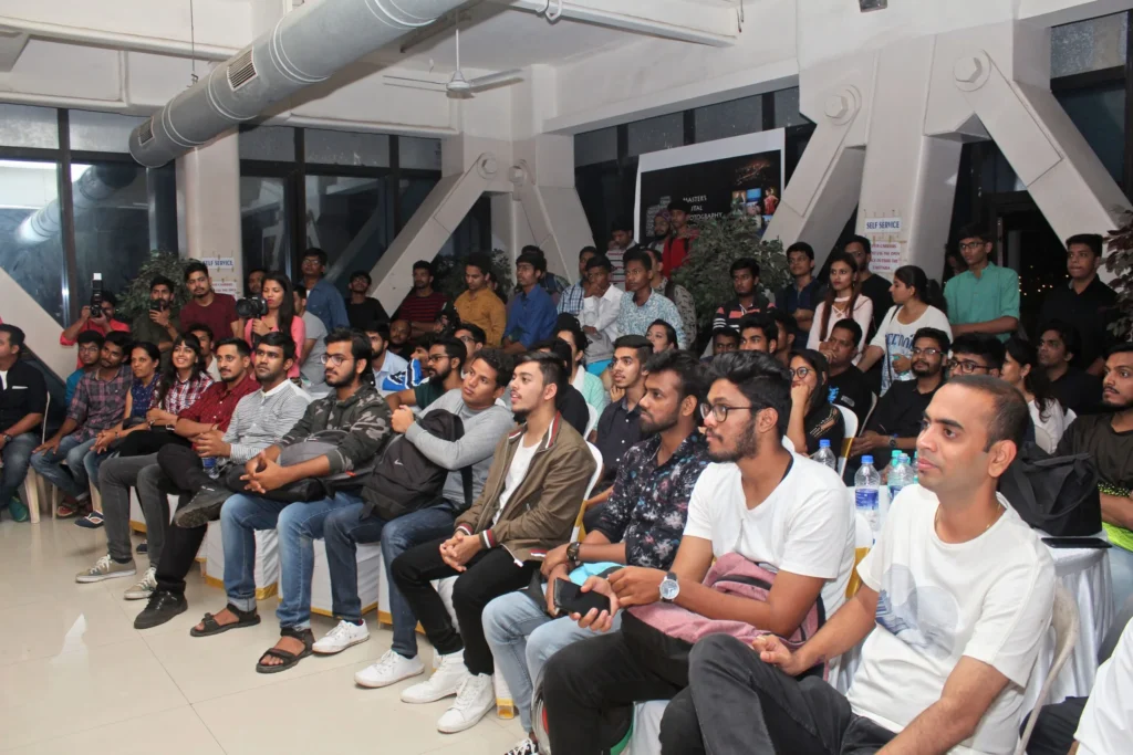 A diverse group of people seated in a well-lit room, engaged in an event or presentation.