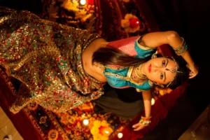 A woman in traditional Indian attire, with long hair and jewelry, posed elegantly against a softly lit background with candles.