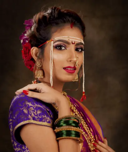 A woman in traditional Indian attire, adorned with jewelry and flowers, poses gracefully with a soft expression.