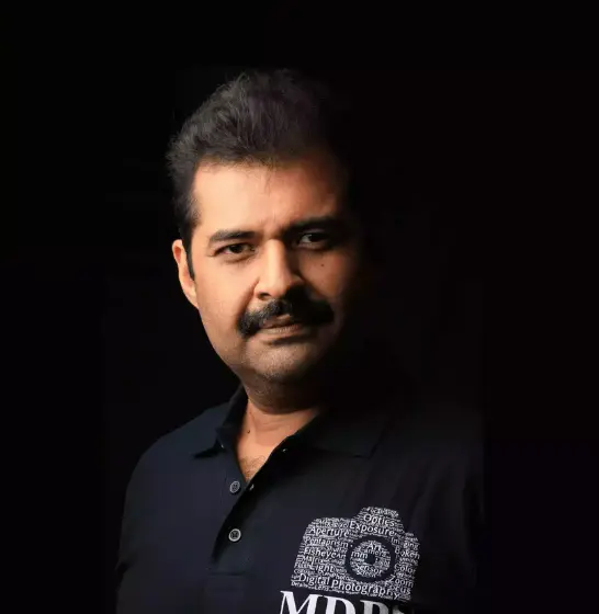 A portrait of a Dharmesh sachde with the face obscured for privacy, wearing a dark polo shirt with the logo “MDPS” embroidered on it, set against a black background.