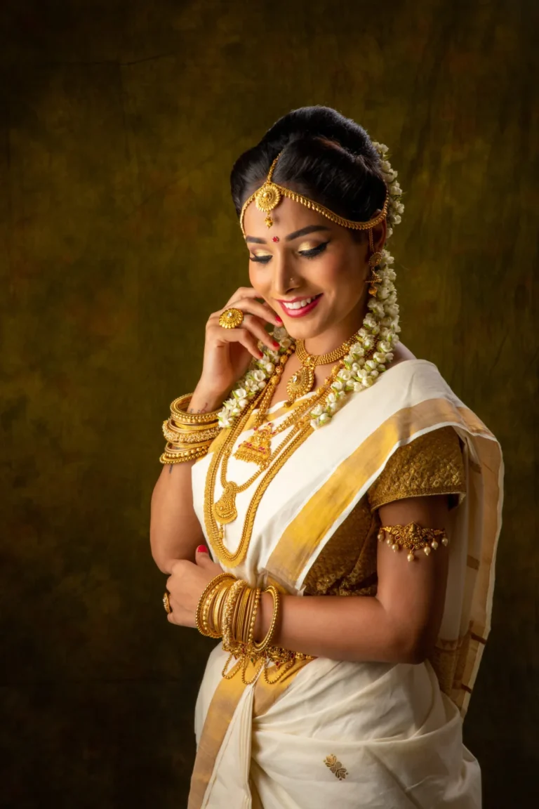 A woman in traditional attire adorned with gold jewelry and floral decorations, smiling gracefully.