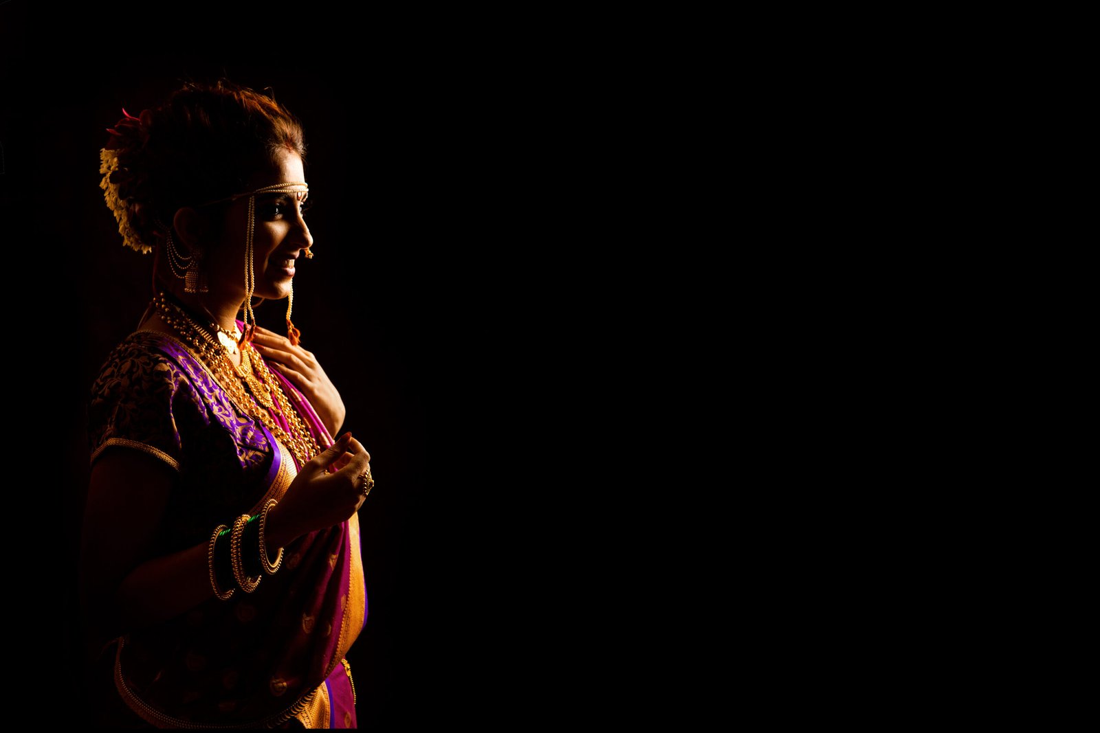 A dramatic, low-key portrait of a bride in traditional Maharashtrian attire with rim lighting against a solid dark background.