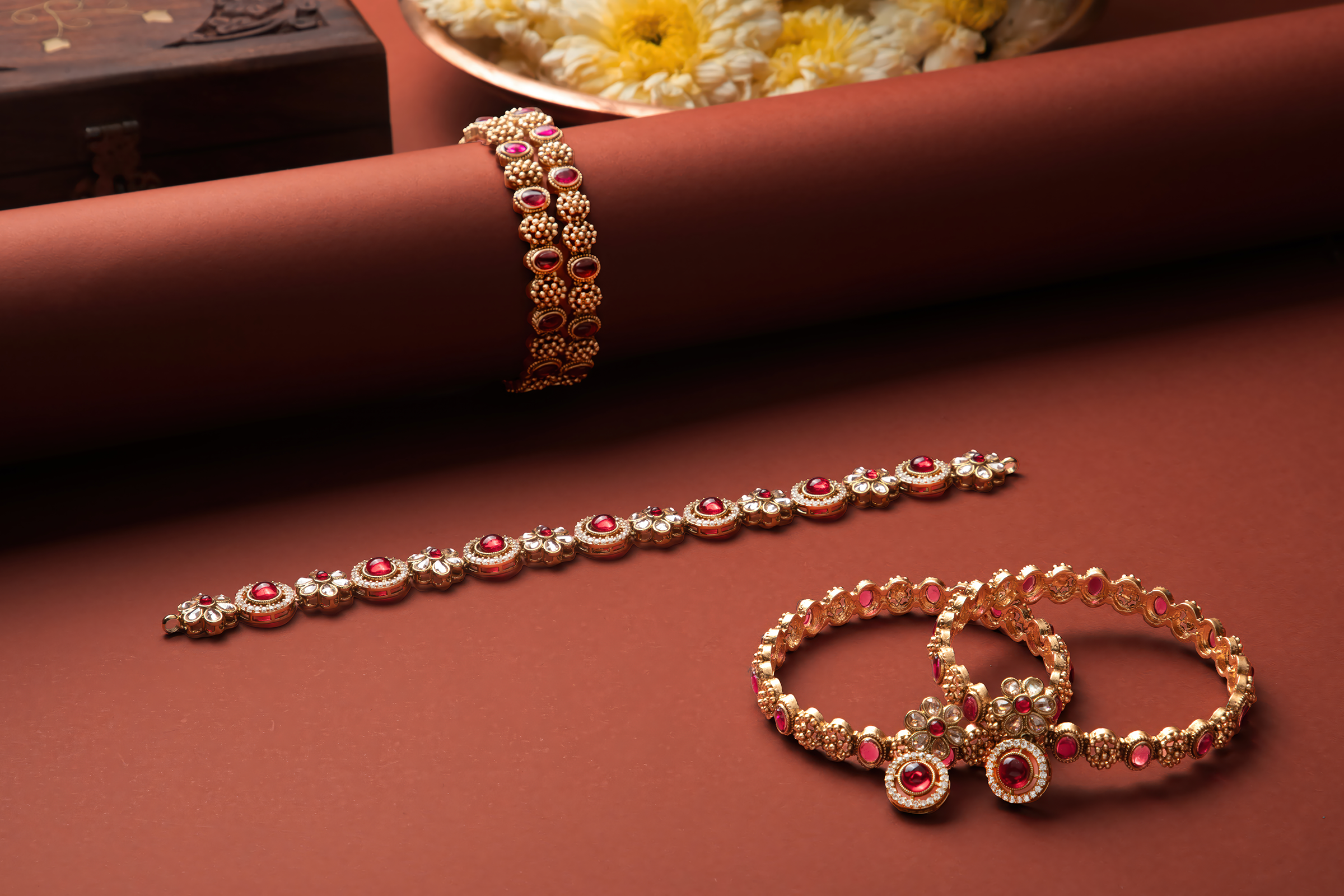 Student commercial jewelry photography project from MDPS featuring gold and ruby bangles styled on a warm brown background.
