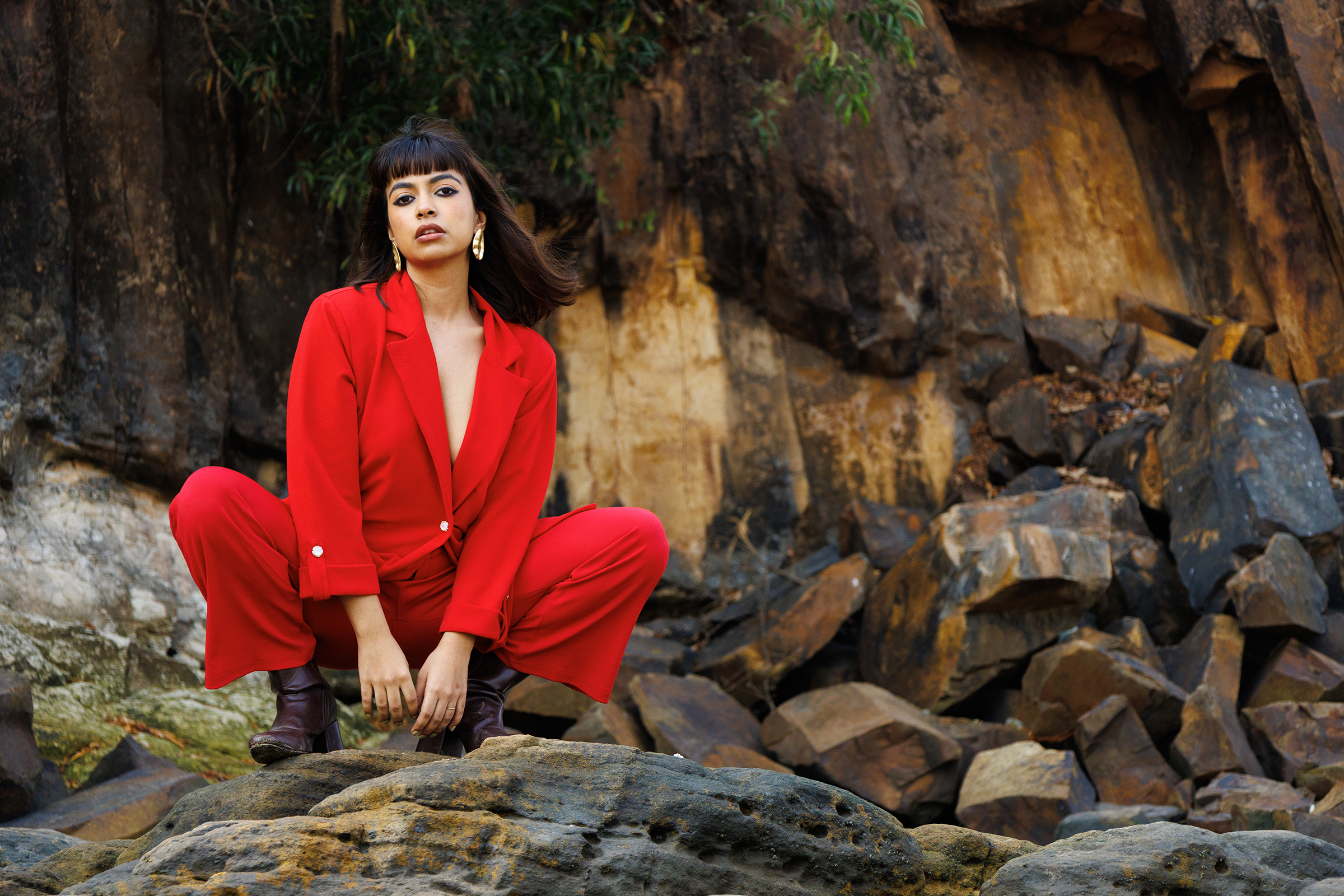 Student high-fashion photography project from MDPS featuring a model in a red pantsuit posing against a rugged rocky cliff face.