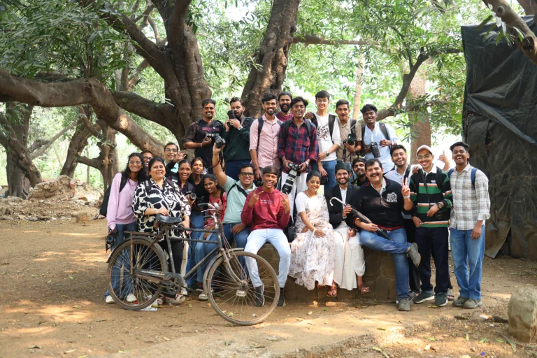 MDPS photography students and mentors gathered outdoors with models and a vintage bicycle during a practical outdoor photography session.