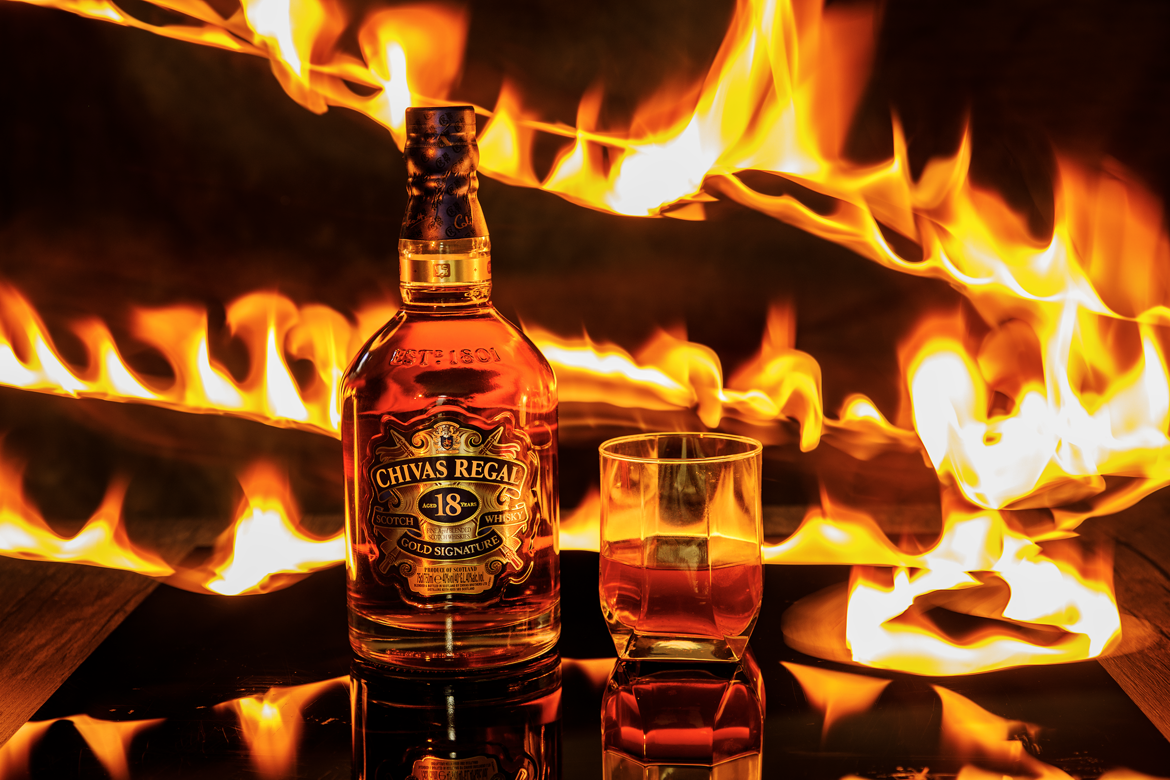 Student commercial product photography project from MDPS featuring a Chivas Regal whisky bottle and glass framed by dramatic fiery light trails.
