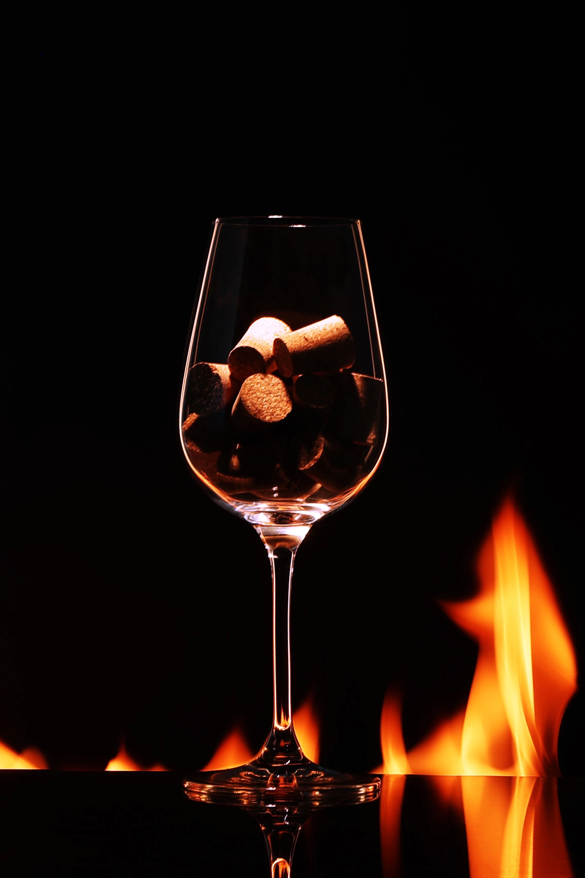 Product photography course student project showcasing a wine glass filled with corks set against a dramatic backdrop of real flames.