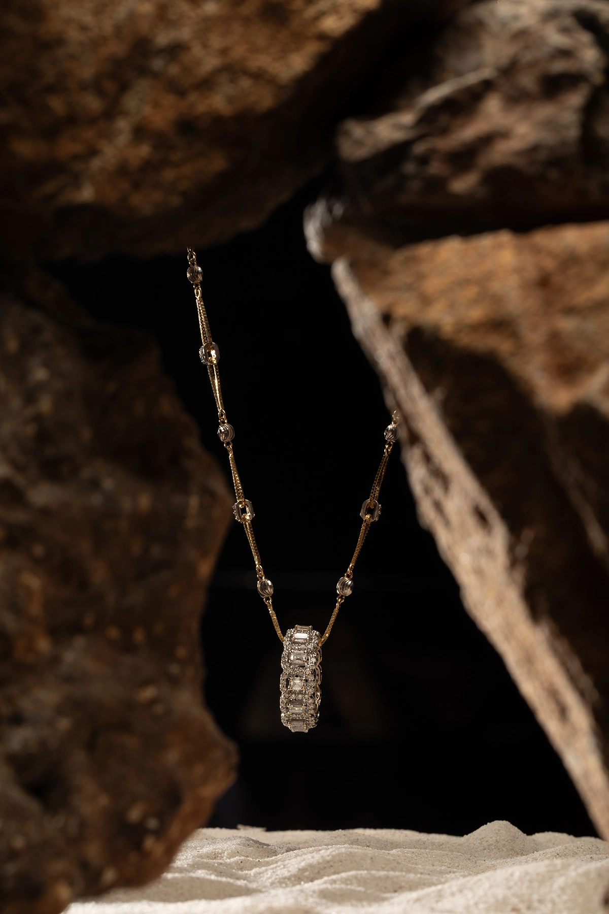 Product photography course student project featuring a diamond and gold necklace suspended between rugged rock textures.