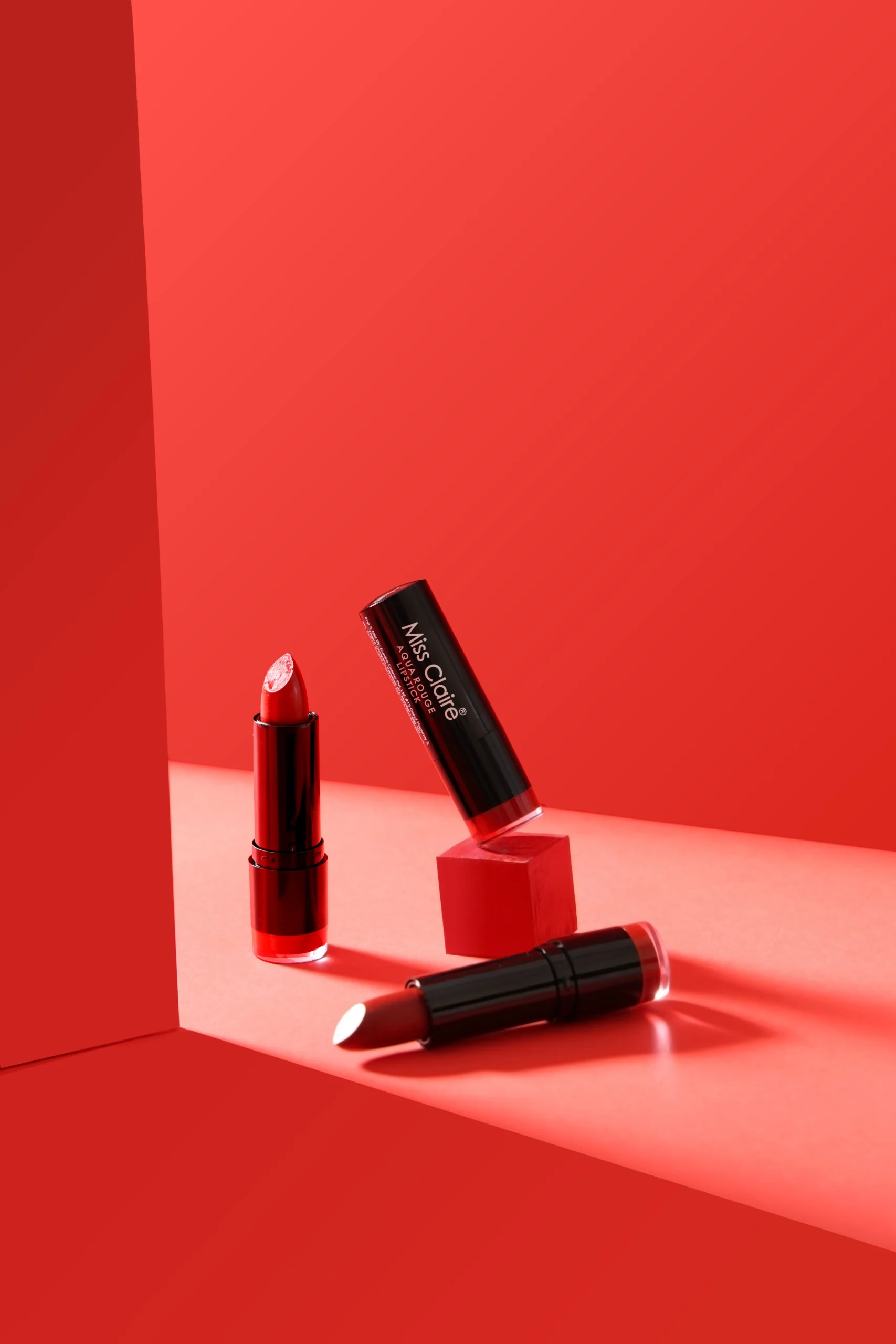 Product photography course student project showcasing red lipstick tubes styled against a vibrant red studio background.
