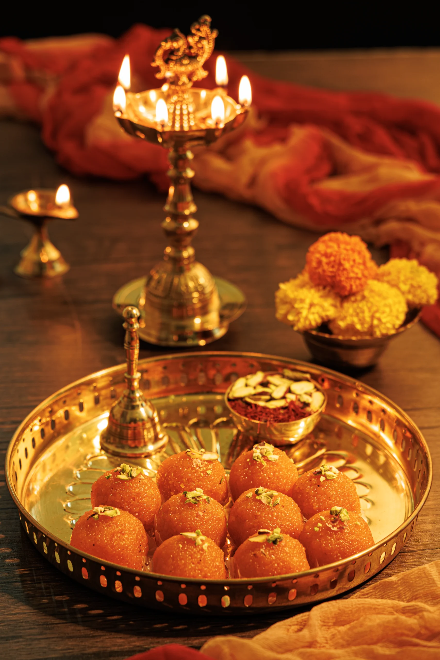 Product photography course student project featuring traditional Indian sweets and a lit brass lamp for festive commercial advertising.
